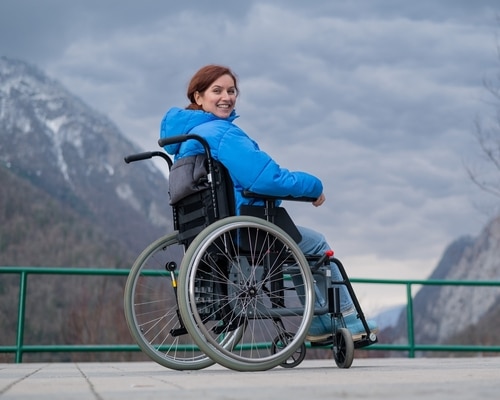 A woman in a lightweight folding wheelchair for travelling smiles over her shoulder with a mountainous landscape in the background.