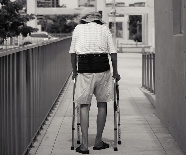 An elderly man walking down a sidewalk using a walker he received from aged care support.