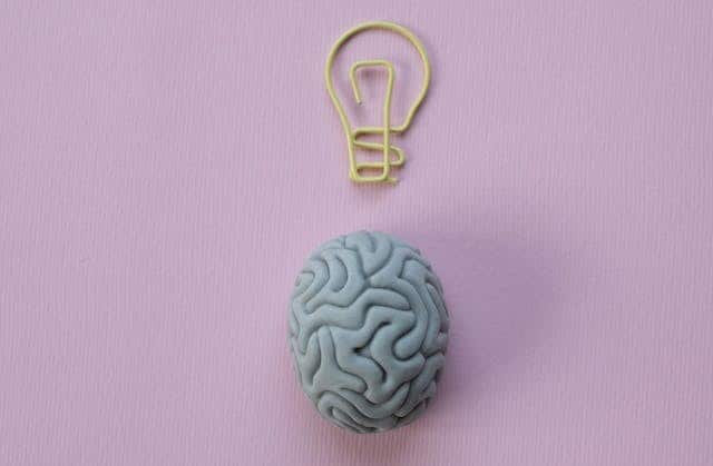 A brain and a light bulb on a pink background inspire creativity and illuminate new ideas, making this image perfect for articles discussing popular blog posts or the experience of living with disability.