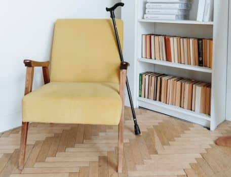 A yellow chair with a cane in front of a bookcase, providing comfort and mobility support for someone with limited mobility.