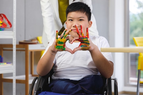 A boy in a wheelchair using adaptive art supplies to create a heart-shaped craft.