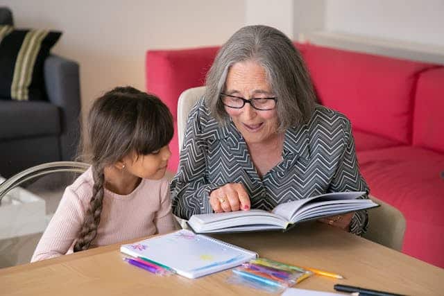 A granny, who may need aged care funding in the next 10 years makes up a component of Australia's baby boomer generation reads a book to her granddaughter 