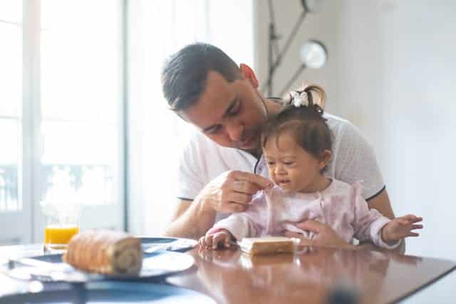 A carer and his daughter eating breakfast at a table.