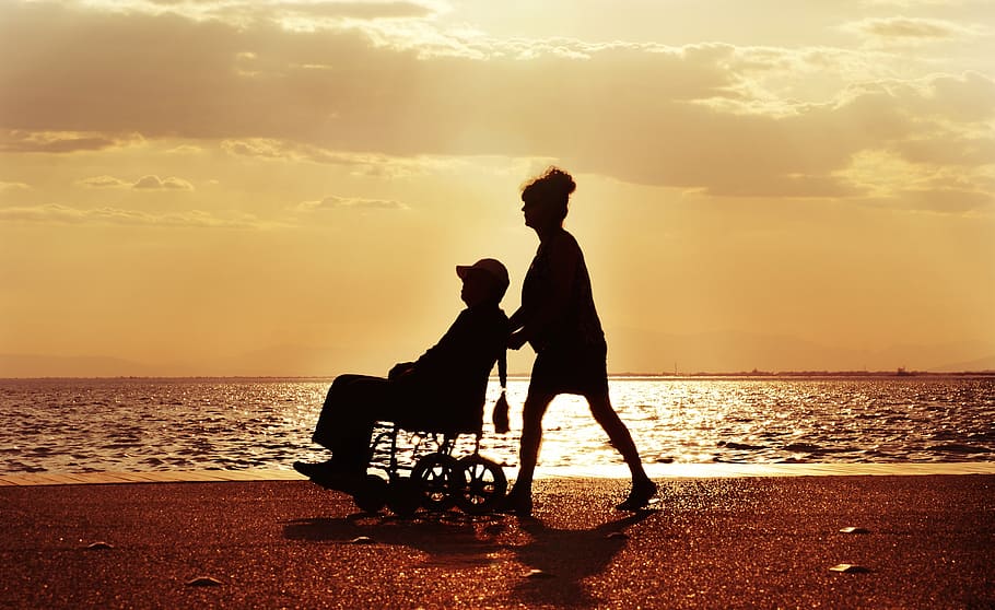 A man and a woman in a wheelchair on the beach at sunset