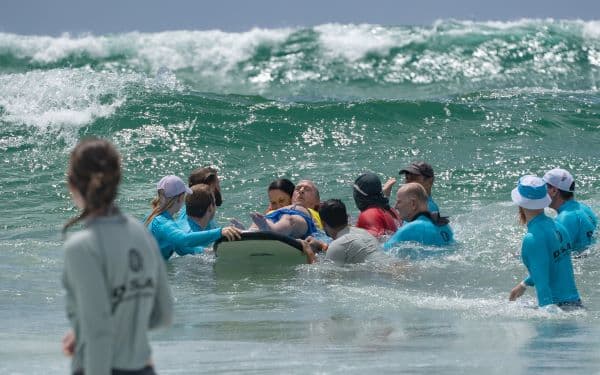 A group of volunteers from the Disabled Surfers Association of Australia support a person to surf with disabilities