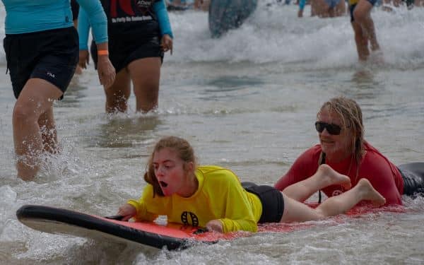 A young girl is learning to ride the waves with the support of volunteers from the Disabled Surfers Association of Australia