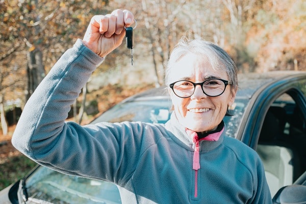Portrait of a happy smiling senior woman learning to drive a car holding the car key to camera