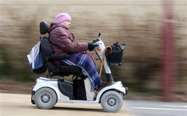 lady in a pink beanie on a mobility scooter whizzing past a brown wall
