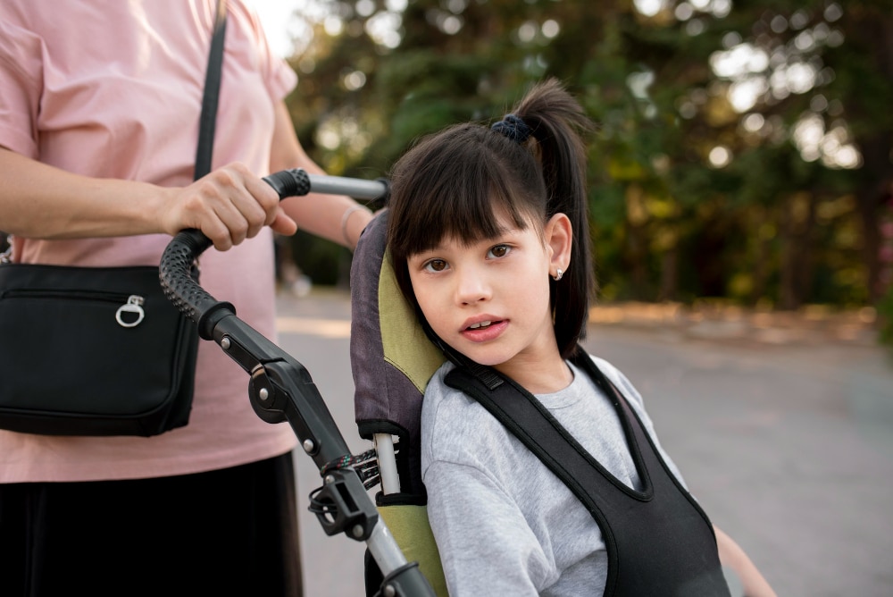 A mum pushes her daugher along in a pediatric wheelchair for a stroll through the park