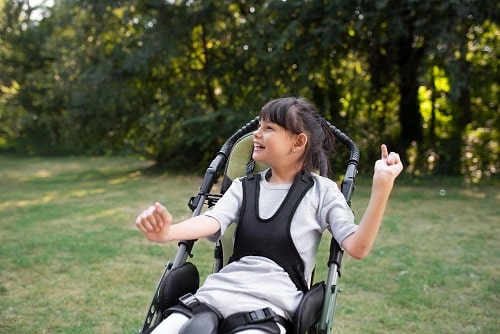 A a young girl smiles happily while sitting in her pram in a grassy park