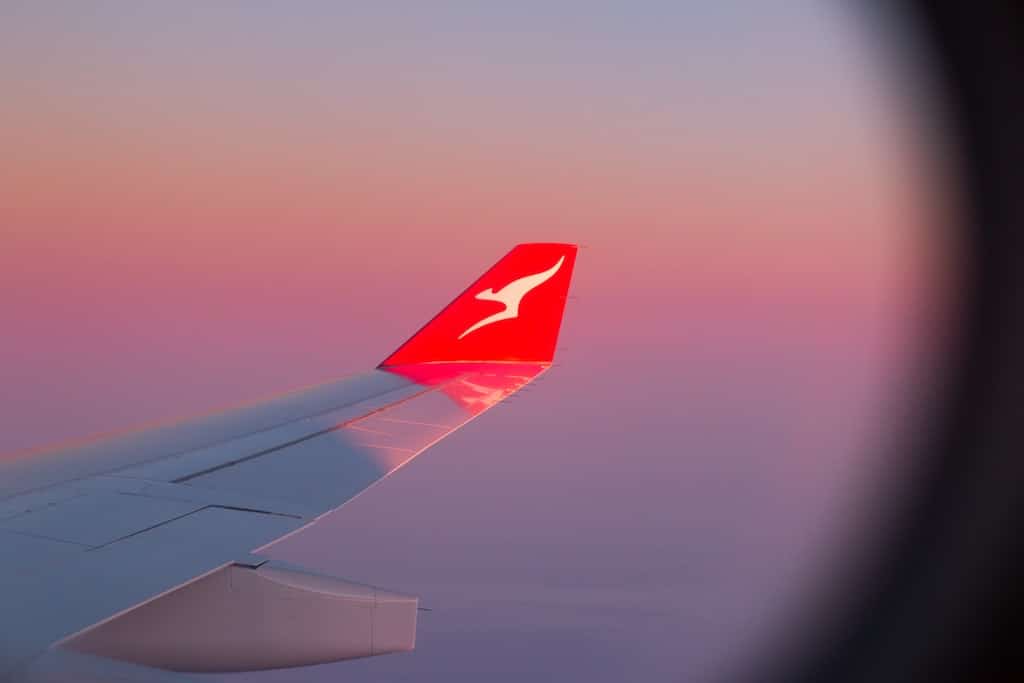 Wing of Qantas plane in the air at sunrise. Qantas offers disability discounts for carers