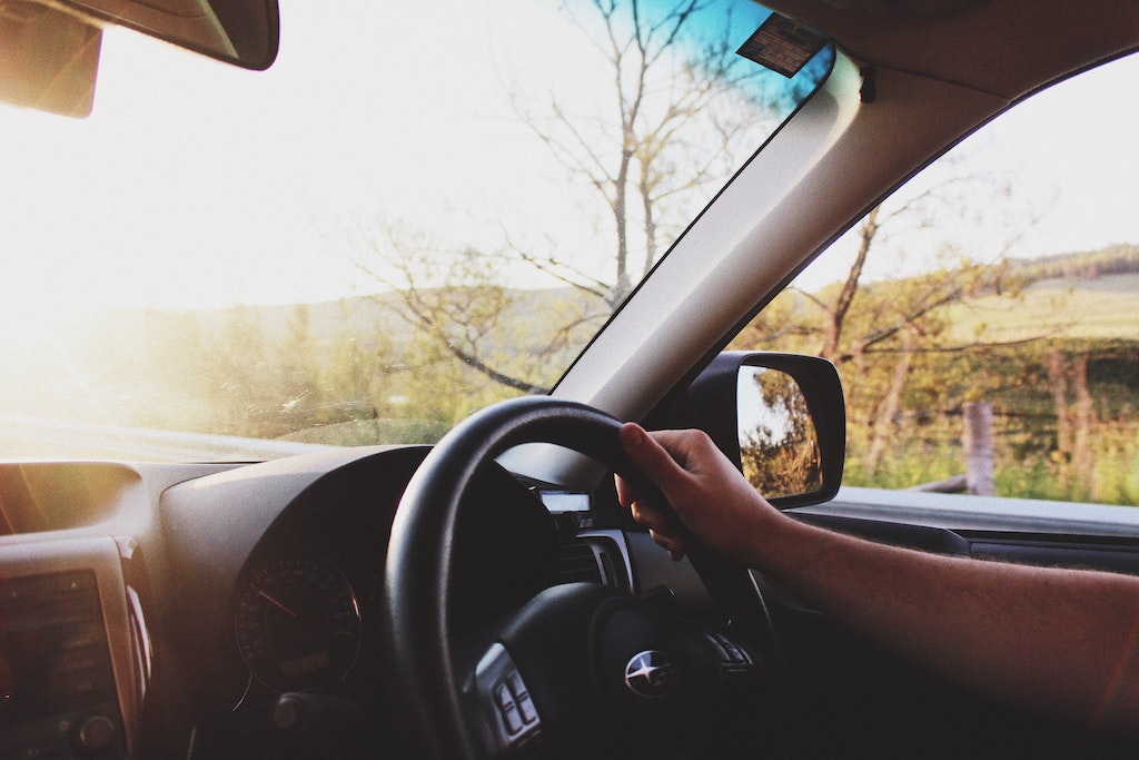 Cut off image of person's hand on steering wheel as they drive through countryside