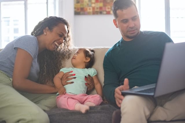 A little girl sits on the couch with her parents who are looking at her NDIS ECEI plan online.