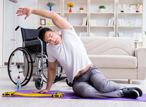 man with limited mobility exercising on mat in front of wheelchair