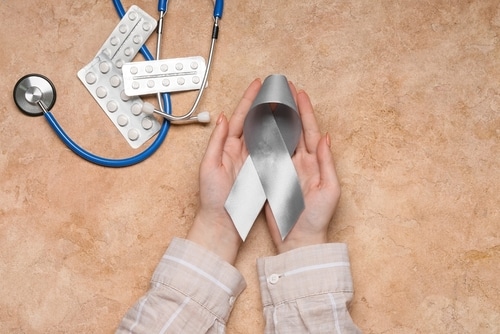 Female hands with Parkinson's Disease awareness ribbon, stethoscope and pills on grunge background