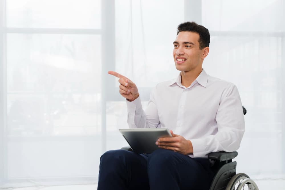 young man in wheelchair holding ipad which can be a helpful gadget for people with disabilities