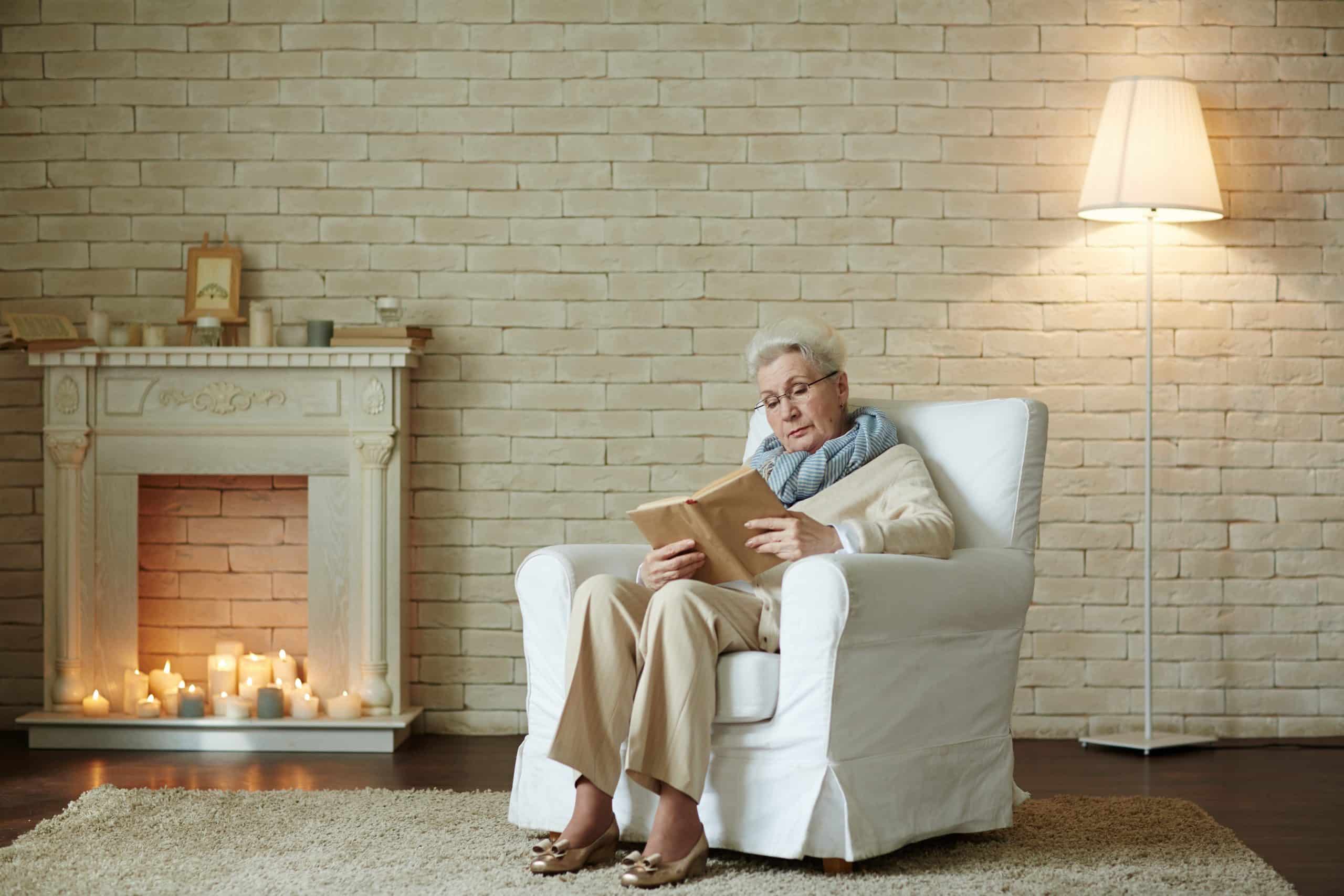 old woman in armchair reading by fire to keep warm in winter