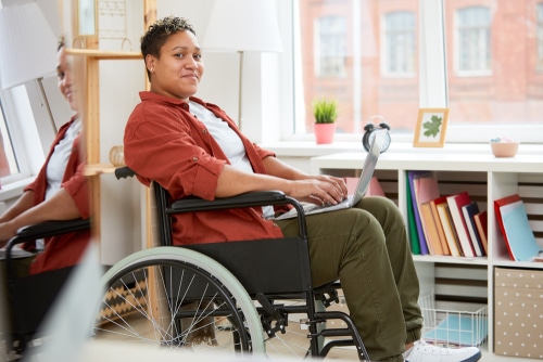 A person in a wheelchair working on their NDIS plan review on a laptop in a bright office space.