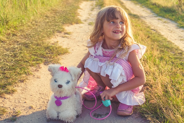 little girl in pink dress playing with plush dog. Girls with autism often have more socially acceptable interests so may be diagnosed late