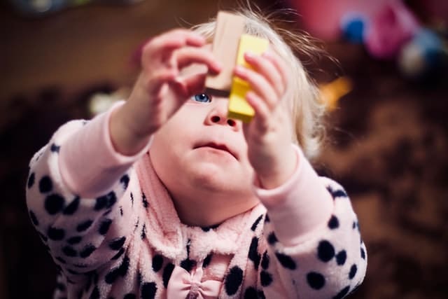 blonde girl toddler playing with two wooden blocks