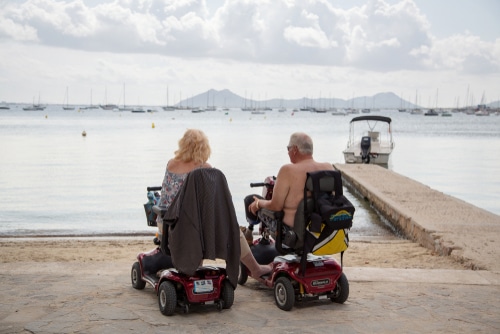 How long do mobility scooter batteries last, wonder this blonde woman and grey haired man on scooters on a path by the beach, looking at water