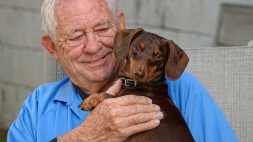 elderly man smiling with Dachshund dog, which can be a good low maintenance pet