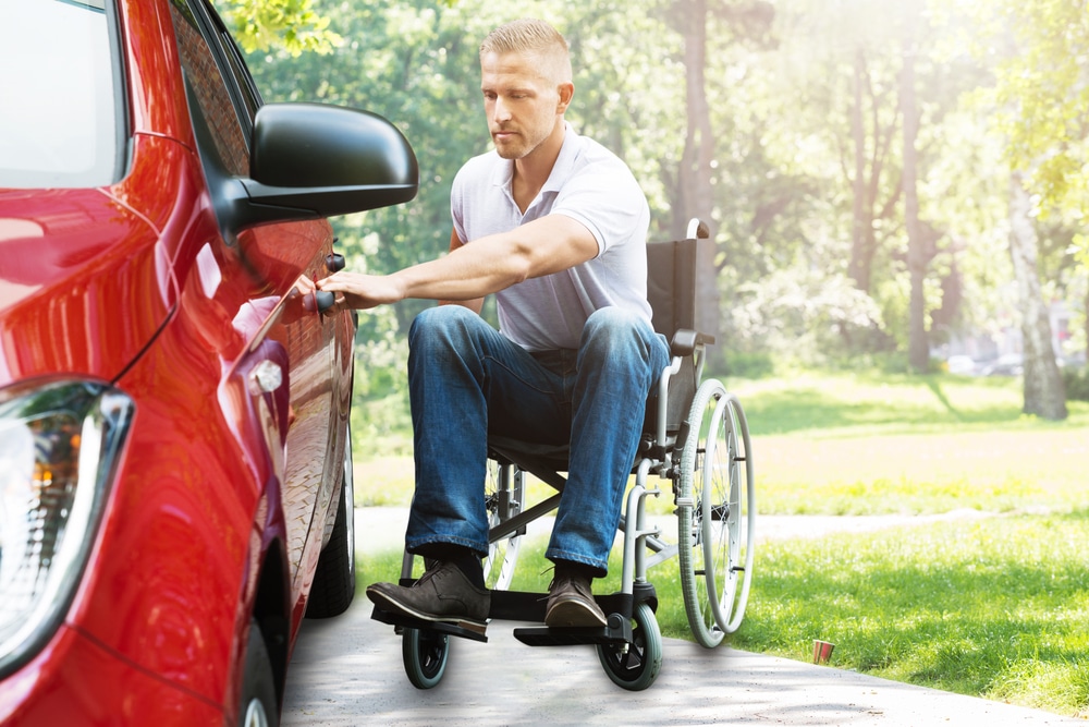 a disability insurance specialist insures this person in wheelchair transferring to car. He may have a disability parking permit