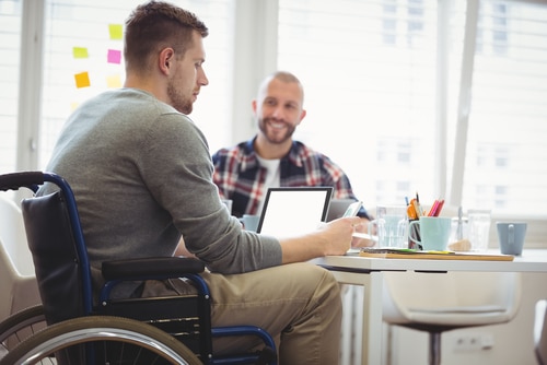 Man in wheelchair with laptop working alongside his NDIS plan manager with phone 