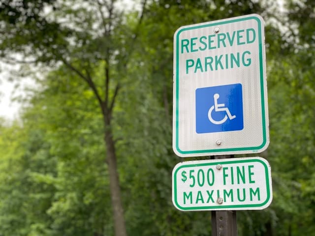        Sign indicating reserved accessible parking bays for people with disabilities, with a notice of a $500 maximum fine for violations. Trees and greenery are visible in the background.