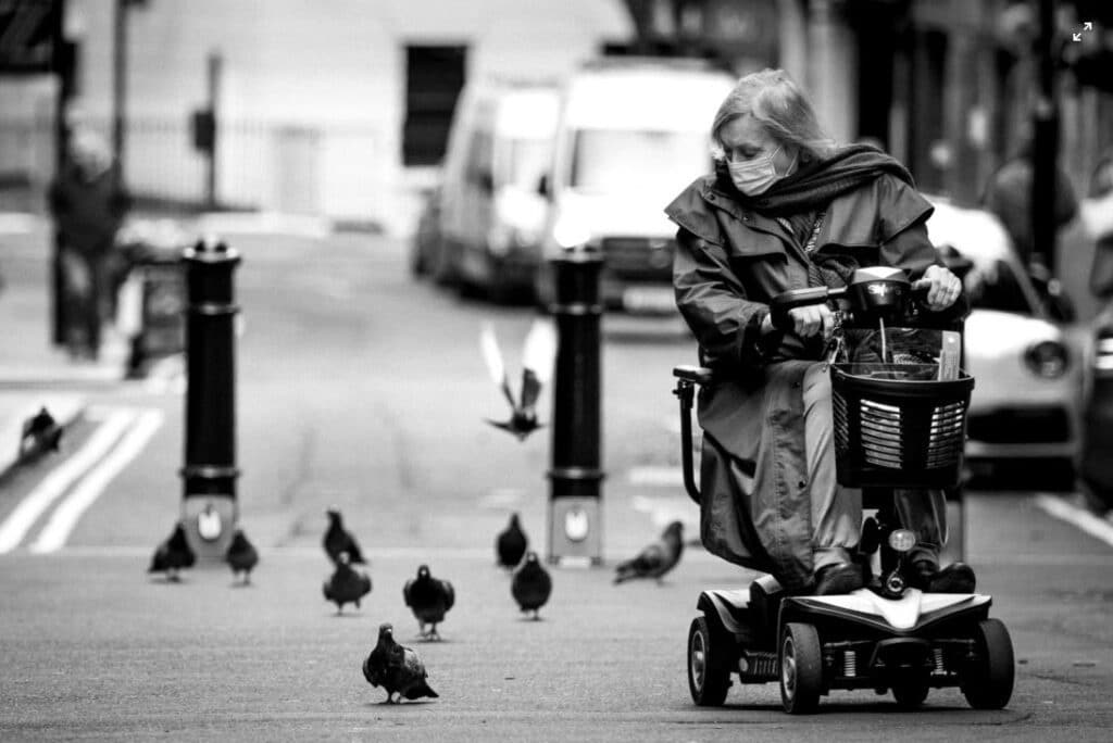 woman on mobility scooter driving around pigeons