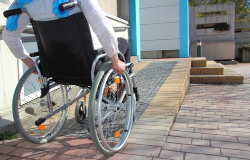 Woman using wheelchair ramp outside home - modifications can be part of an occupational therapy assessment report