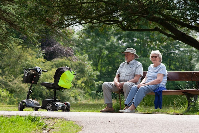 Two elderly people sitting on a bench with their mobility scooters park. A stolen mobility scooter can be devastating
