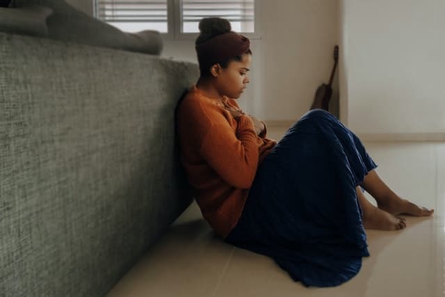 woman with anxiety sitting with back against couch and hands on chest