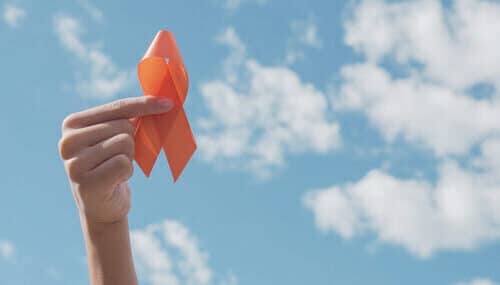 hand holding an orange ribbon for multiple sclerosis (MS) awareness against blue sky with clouds