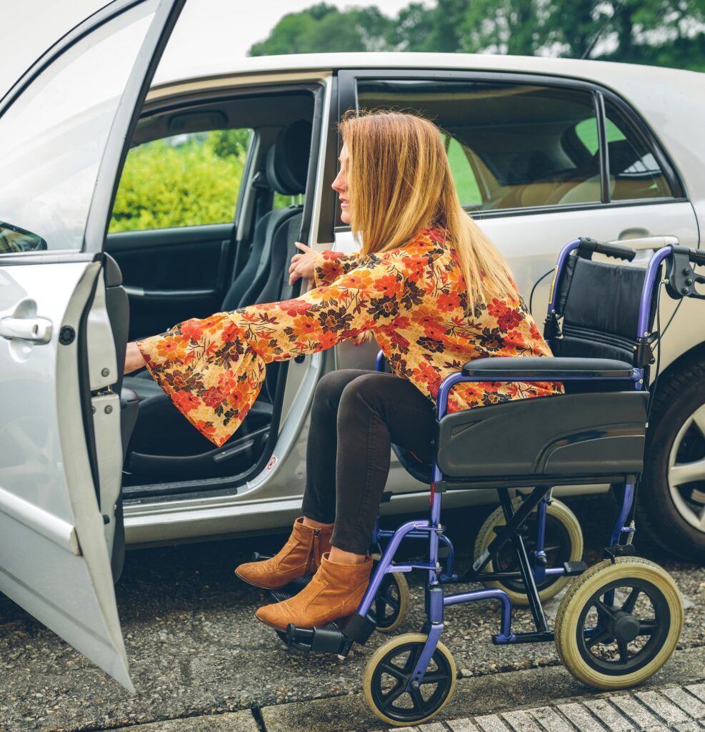 woman in wheelchair transferring into passenger side of silver car