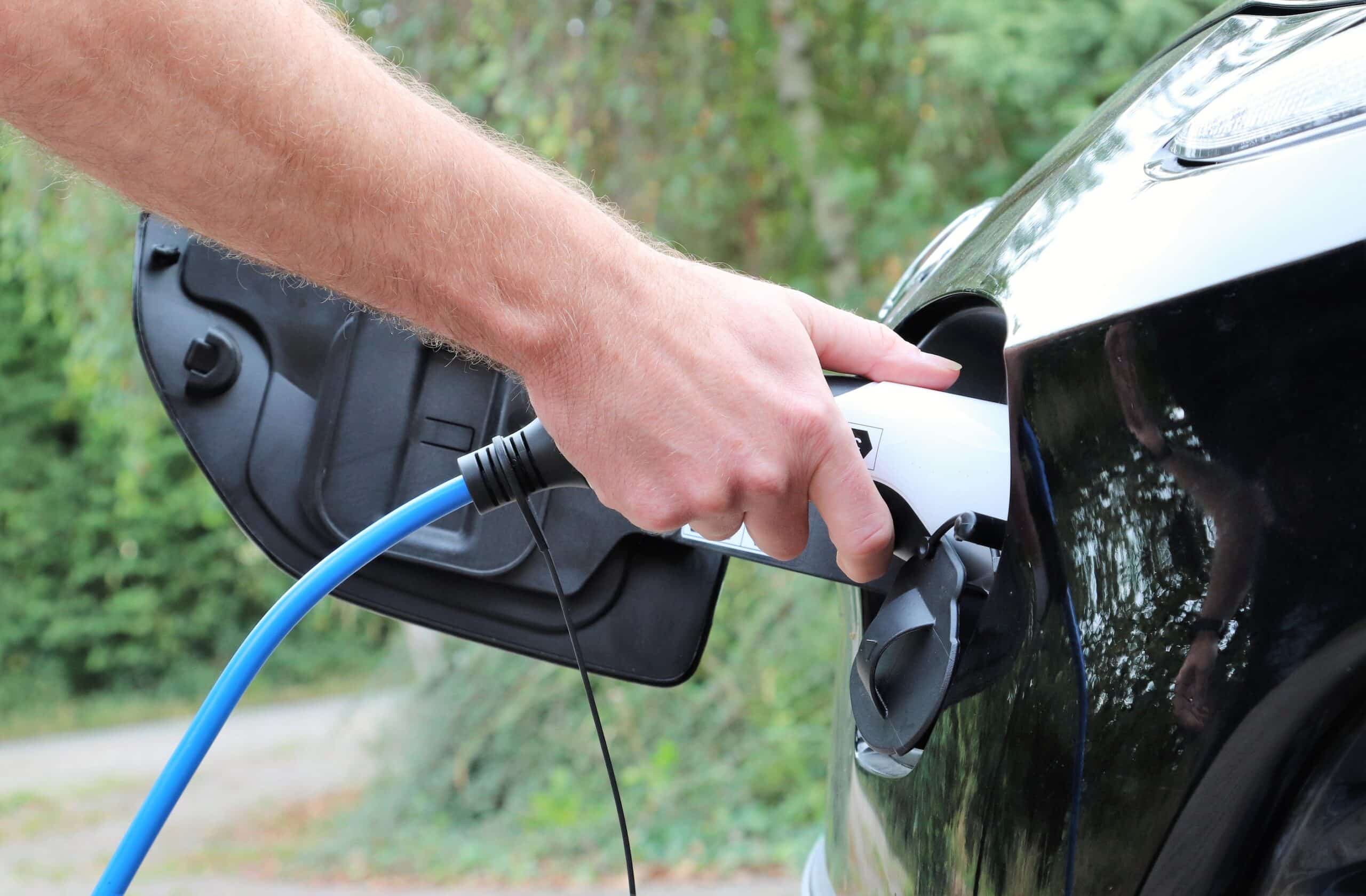 close up of man's hand plugging in charging cable to electric car