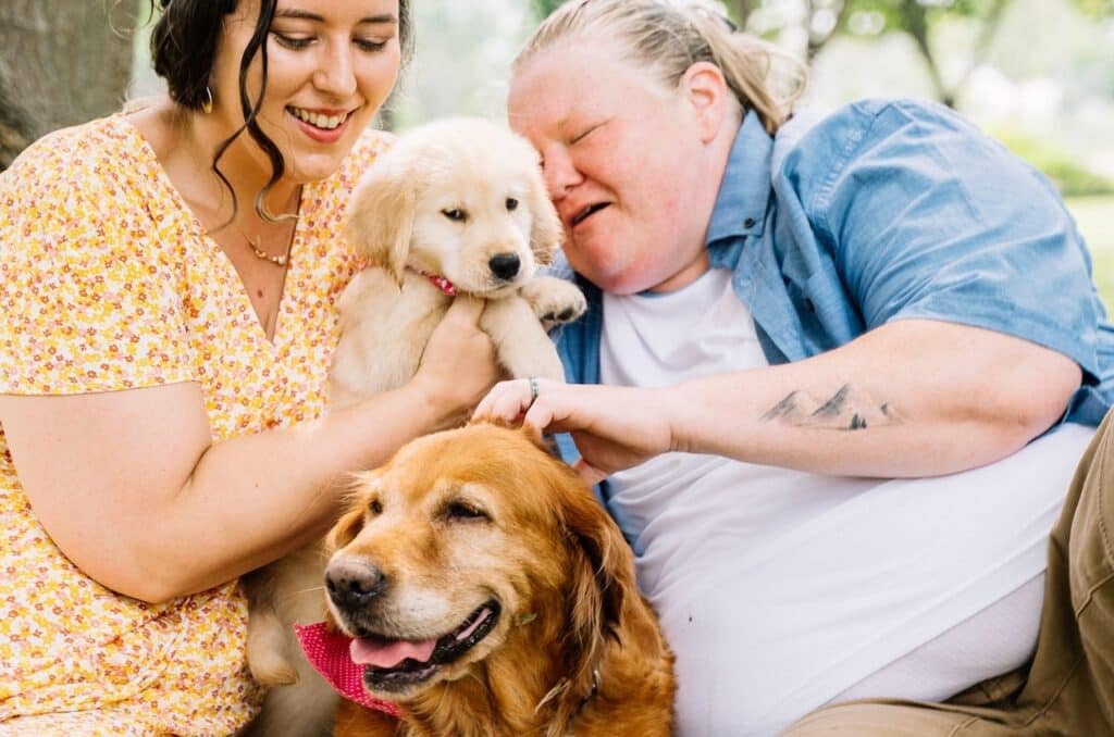 A trainer is holding a puppy up to a woman with autism spectrum disorder while training the puppy to become an Assistance Dog