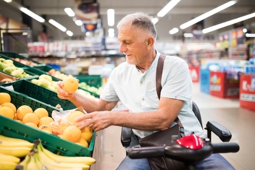 older man in mobility scooter at grocery store picking fruit up. Mobility scooter insurance should cover your scooter away from home too