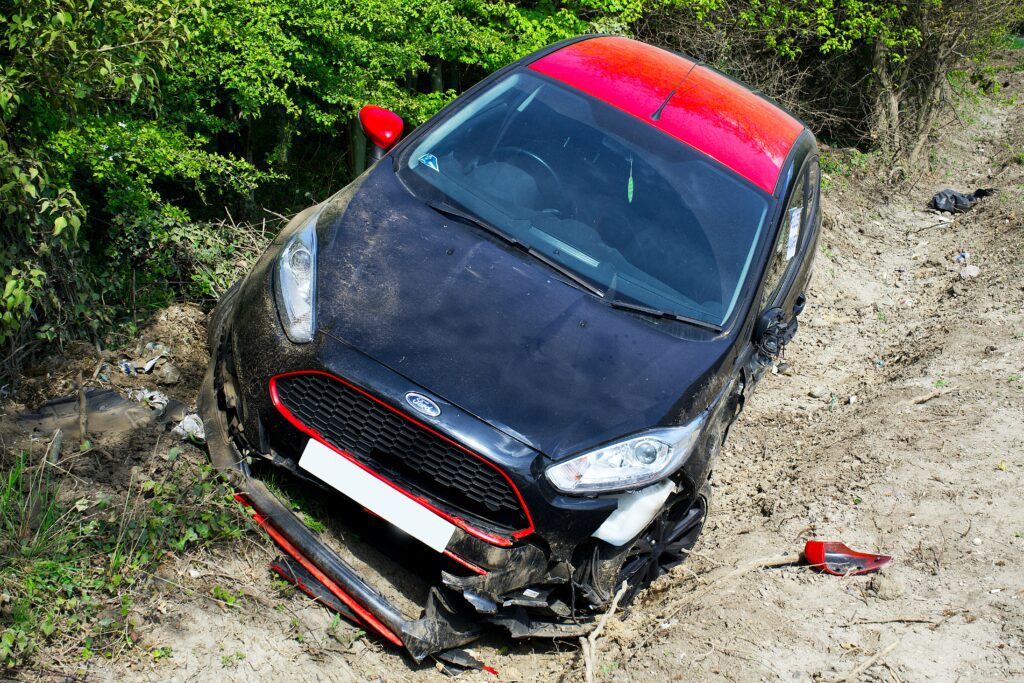 A red car crashed into a ditch. You should avoid driving without insurance because getting into a car accident with no insurance can lead to a hefty financial burden on you.