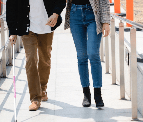 A woman assisting a man walking with a cane, he may be suffering from dementia and mobility issues.