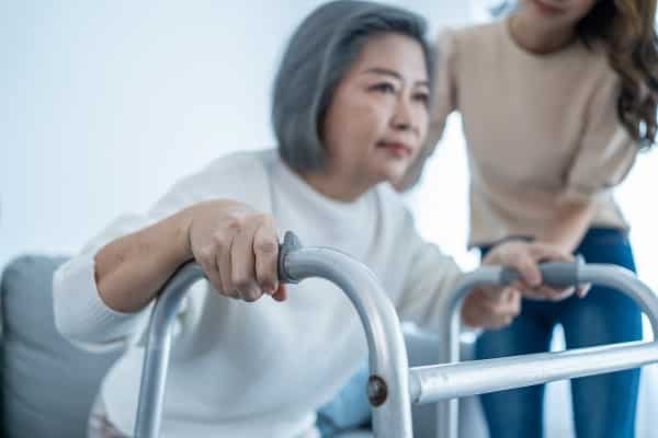 A young woman helping and elderly woman use her walker, she may be suffering from dementia and mobility issues.