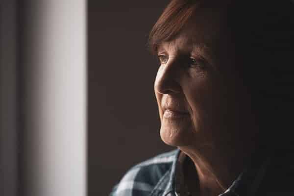 An elderly woman looking out of a window, she may be suffering from dementia and mobility issues.