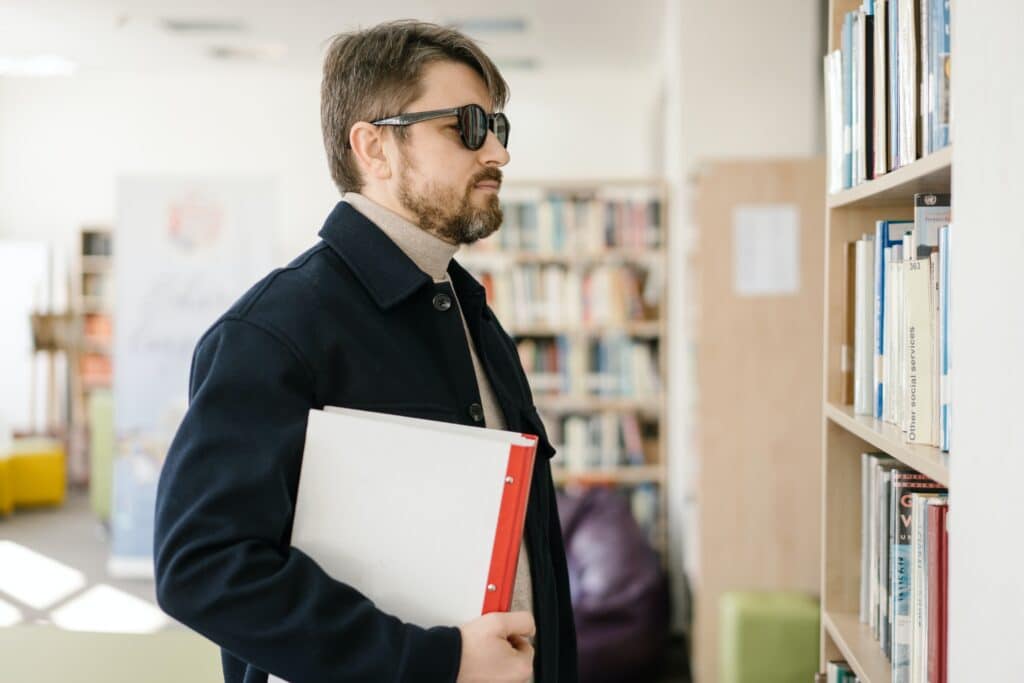 “What are my rights when it comes to disability in the workplace” wonders this visually impaired man with a black jacket and dark glasses who's facing books on a bookshelf