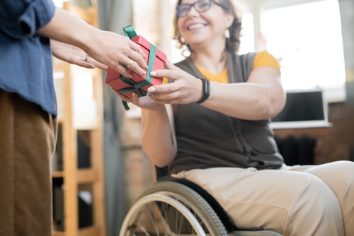 It's time for Christmas activities like gift shopping for kids and adults with disabilities. This photo of a wheelchair using woman taking a present demonstrates gift ideas for disabled people