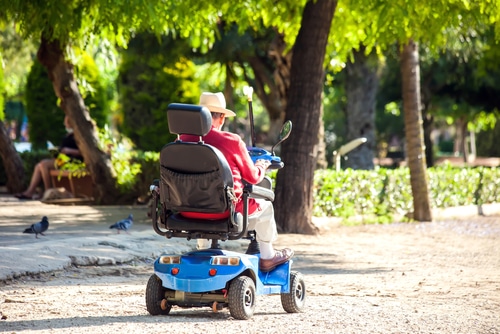 A mobility scooter battery needs to be charged regularly so you can get on with life like this man in a red shirt on his mobility scooter with trees around. 