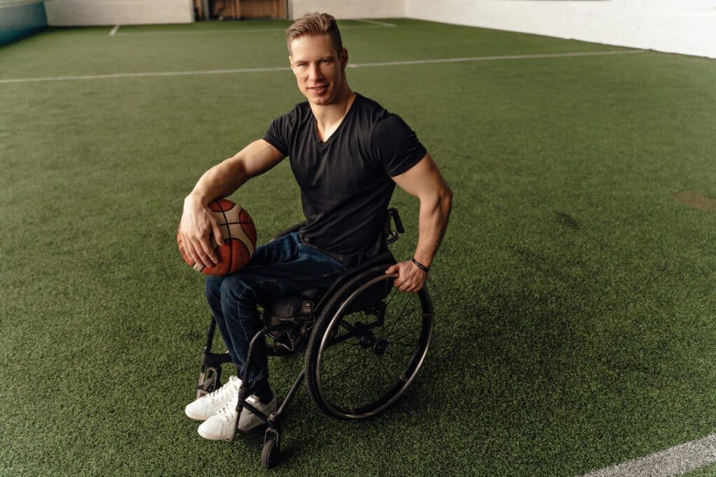 A man sits on a wheelchair holding a ball.
