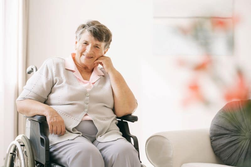 "What is Alzheimer’s disease & how does dementia differ?" wonders this smiling older woman in grey in a wheelchair, knowing it causes the brain to shrink and can reduce cognitive and physical ability