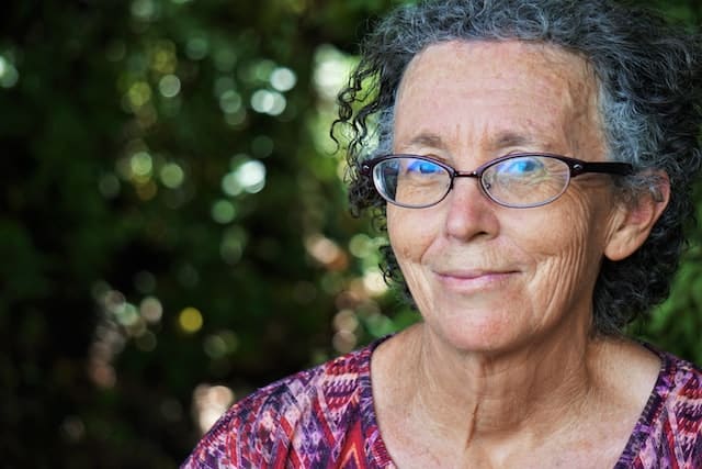 older persons, like this grey haired lady with glasses and a pink shirt looking at the camera, deserve more from the Aged Care Scheme