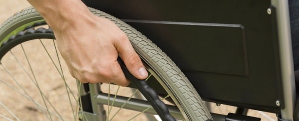 Closer shot of a disabled man's hand leaned on the wheel of his wheelchair. Some patients require bariatric wheelchairs or heavy duty wheelchairs