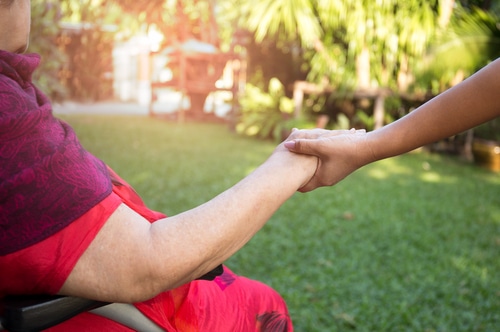 Two women holding hands, one is in a wheelchair. She may be in a Bariatric Wheelchair or heavy duty wheelchair.